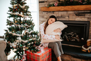 woman hugging pillow next to Christmas tree. Sitting by fireplace.
